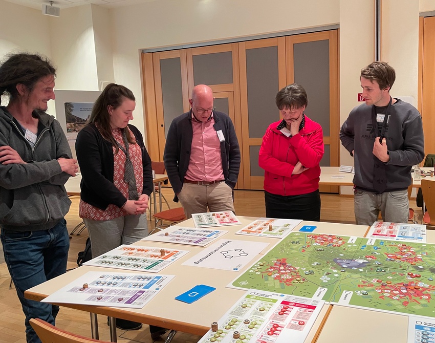 fünf Personen stehen um einen Tisch mit einem Spiel