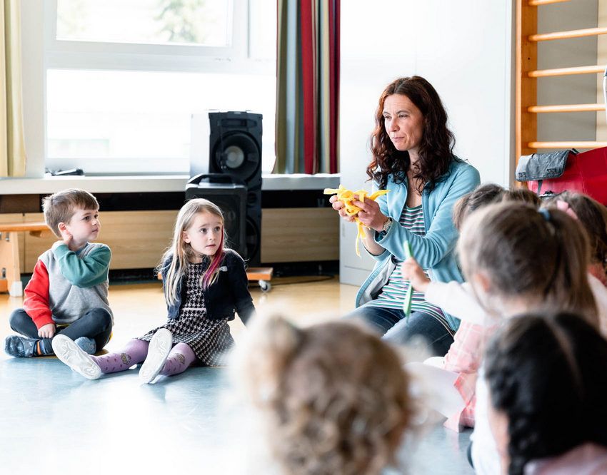 Eine Schulklasse sitzt im Kreis. Die Lehrkraft erklärt etwas.