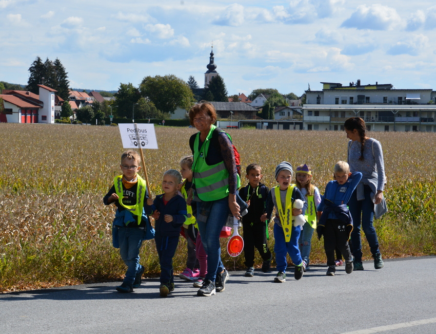 Eine Gruppe von Kindern gehen mit zwei Erwachsenen entlang eines Felds auf der Straße