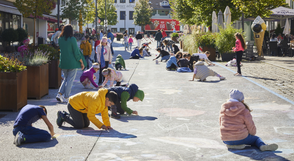 Kinder malen mit Kreide in der Klimabündnis gemeinde Wattens auf der Straße bei Sonnenschein