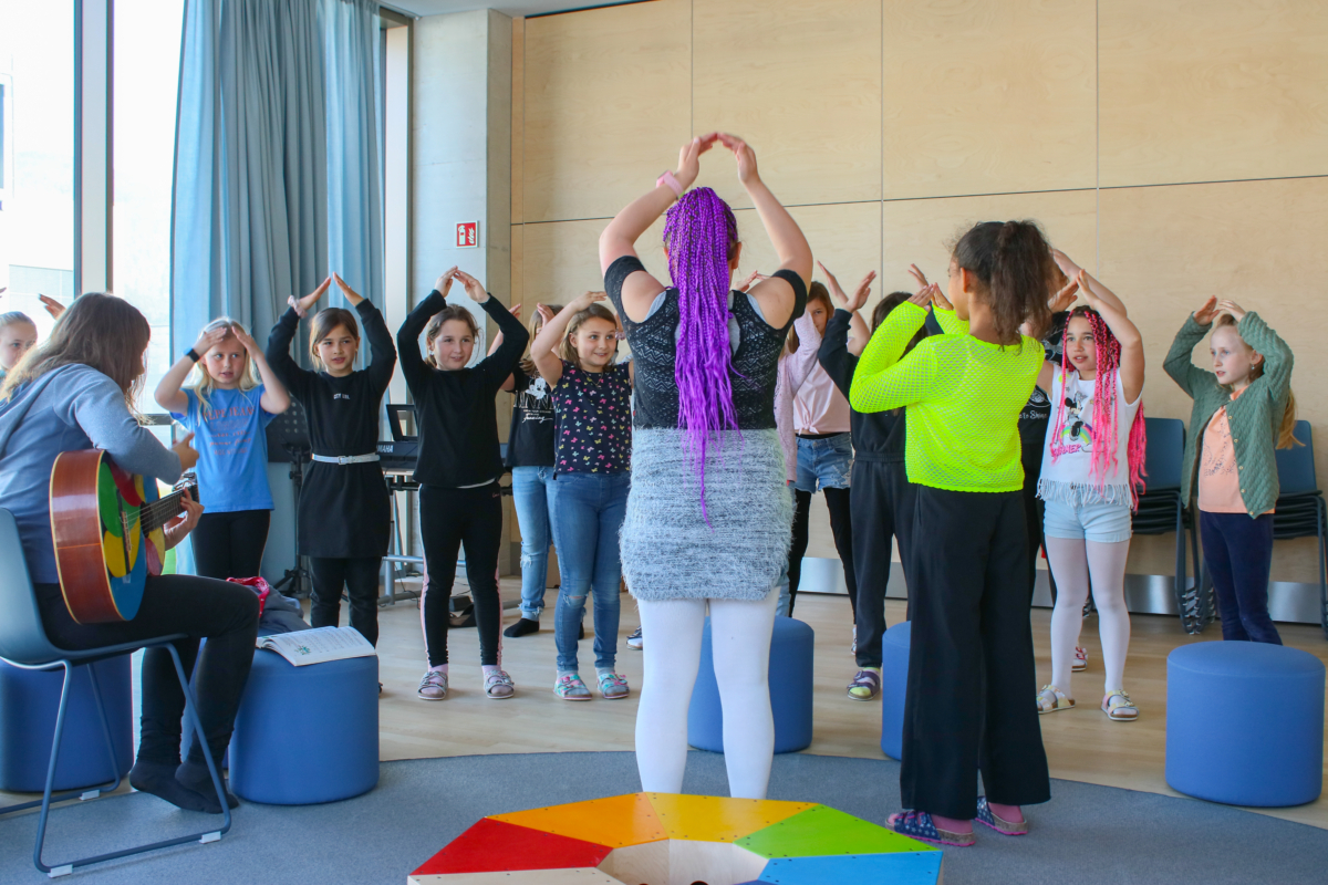 Kinder stehen in Turnhalle und Singen zu dem Gitarrenklängen eines Lehrers