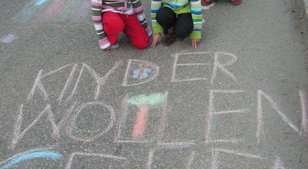 Kinder mit Schrift auf mit Straßenmalkreide "Kinder wollen gehen"