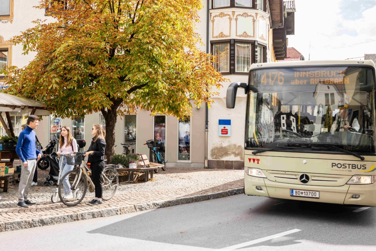 3 Personen auf Gehsteig und Bus