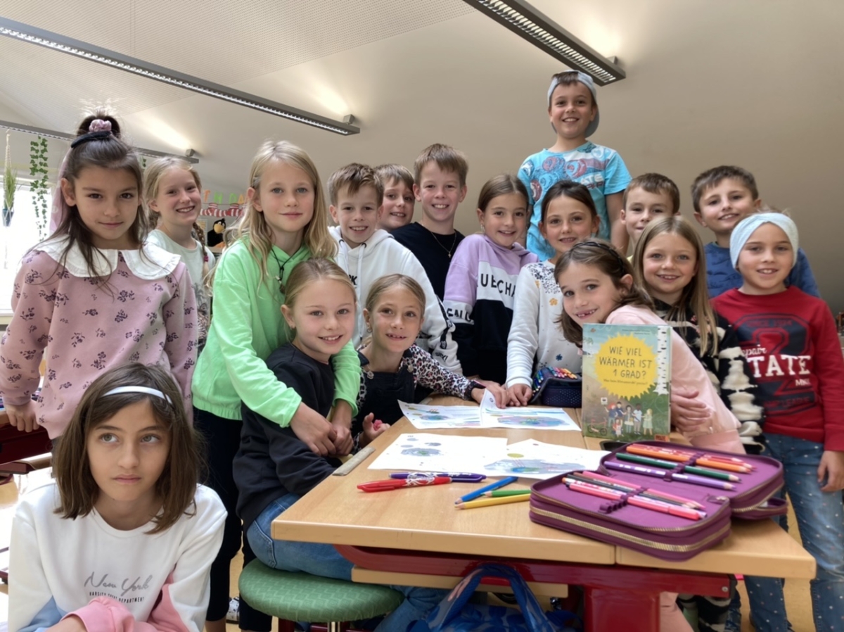 Kinder der Schule und Klimabündnismitglied sitzen um Tisch mit Büchern zum Thema Nachhaltigkeit