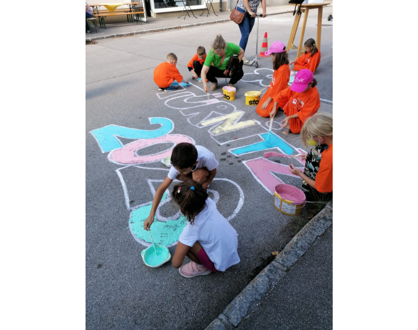 Kinder sitzen malend auf der Straße und zeichnen mit Kreide auf den Asphalt