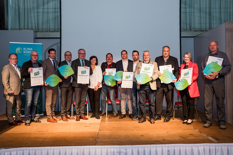 20 Menschen stehen auf einer Bühne mit den Klimabündnis-Jubiläumsurkunden.