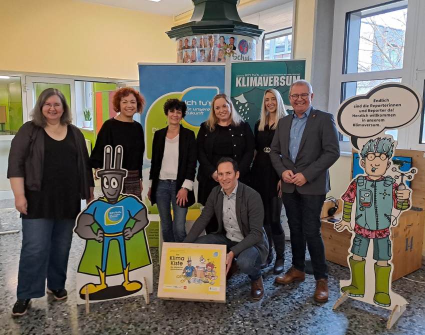 Gruppenbild mit Roll-Ups zu KLIMAVERSUM und Ichtus's Initative, mit der Klimakiste im Vordergrund und zwei Klimachecker-Pappfiguren. v.l.n.r.: Andrea Hairass – Direktorin der Friedrich Aduatz Mittelschule Voitsberg, Cornelia Schweiner – Bildungsreferentin Land Steiermark (Abteilung 15), Claudia Nestler – Stadtbücherei Voitsberg, Tanja Gössler – Pädagogin Friedrich Aduatz Mittelschule Voitsberg, Martina Benedikt – Stadtgemeinde Voitsberg, Bernd Osprian – Bürgermeister Voitsberg, vorne: Fritz Hofer – Geschäftsführer Klimabündnis Steiermark
