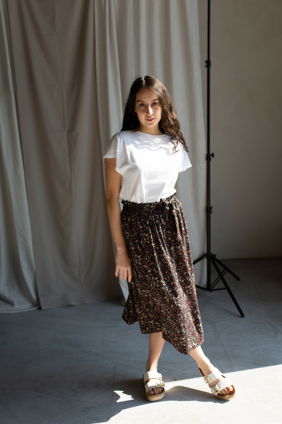 Model mit Rock und T-Shirt steht vor Vorhang