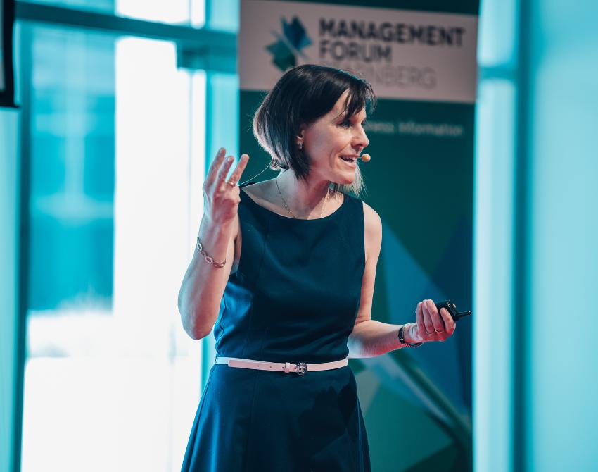 Evelyn Raht mit blauem Kleid vor einem Roll-Up des Management Forums