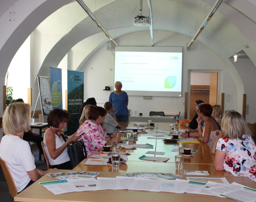 Teilnehmerinnen sitzen am Tisch und schauen auf eine Leinwand, vor der Steffi Greiter vom Klimabündnis Steiermark steht und referiert.