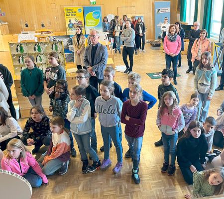 Eine Gruppe von Kindern, im Hintergrund Cornelia Schweiner und Stationen der Klimaversum Wanderausstellung