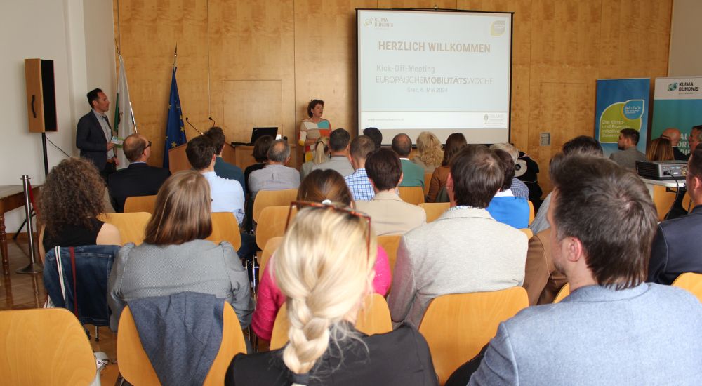 Ursula Lackner, Landesrätin für Umwelt, Klimaschutz, Energie, Regionalentwicklung und Raumordnung steht neben einer Leinwand. Das Publikum ist von hinten sichtbar und schaut auf sie.