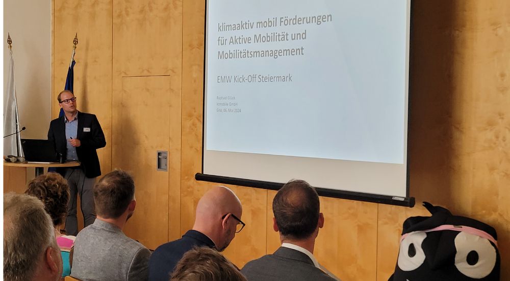sitzendes Publikum schaut auf vortragende Person und Leinwand