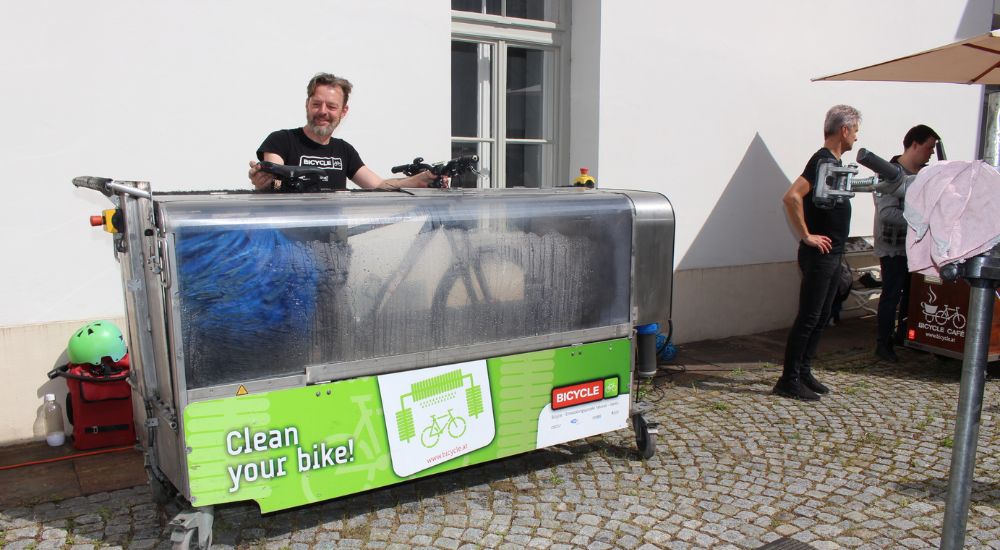 Fahrrad in Box, die eine Fahrradwaschlanlage ist. Dahinter steht eine Person