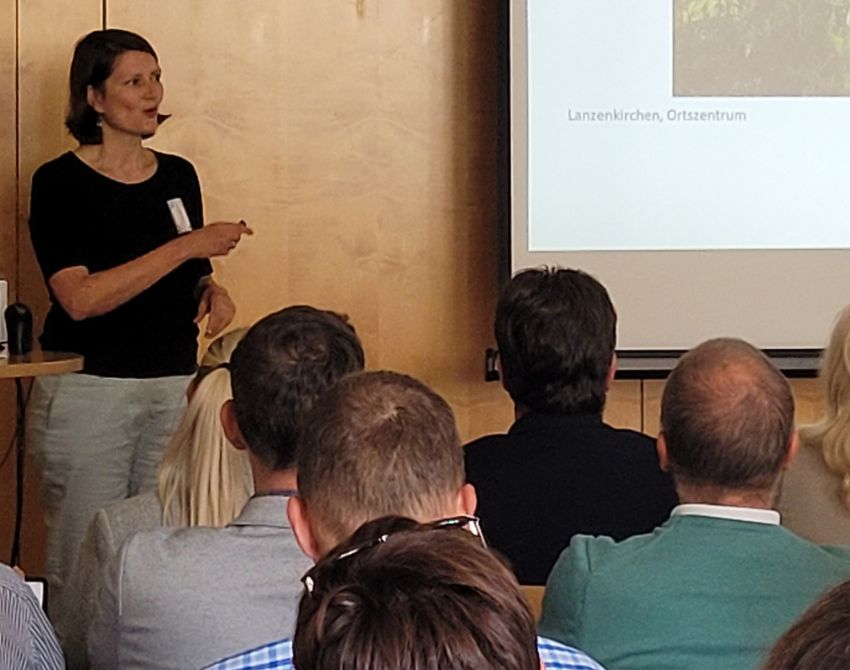 Dr. Eva Schwab bei ihrem Impulsvortrag zu aktiver Mobilität als Input für die für die Europäische Mobilitätswoche 2024, neben ihr eine Leinwand, das sitzende Publikum ist von hinten sichtbar und schaut auf sie,