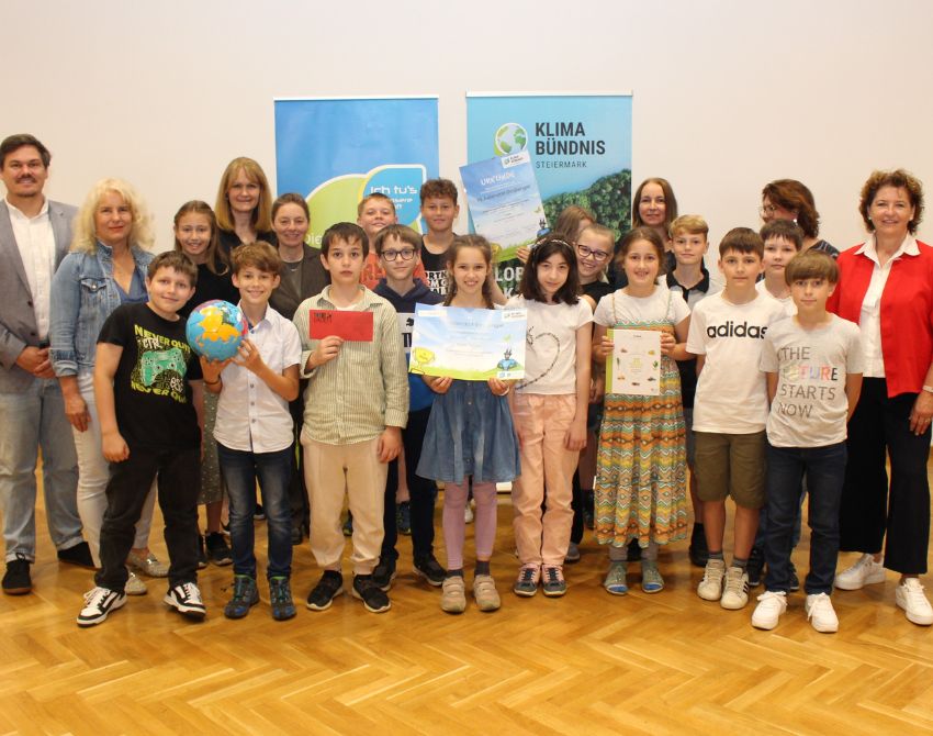 Gruppenbild von Kindern mit Urkunden, einem großen Scheck und Gutscheinen in der Hand, und einem Fußball, mit Erwachsenen am Bildrand, dahinter zwei Roll-Ups