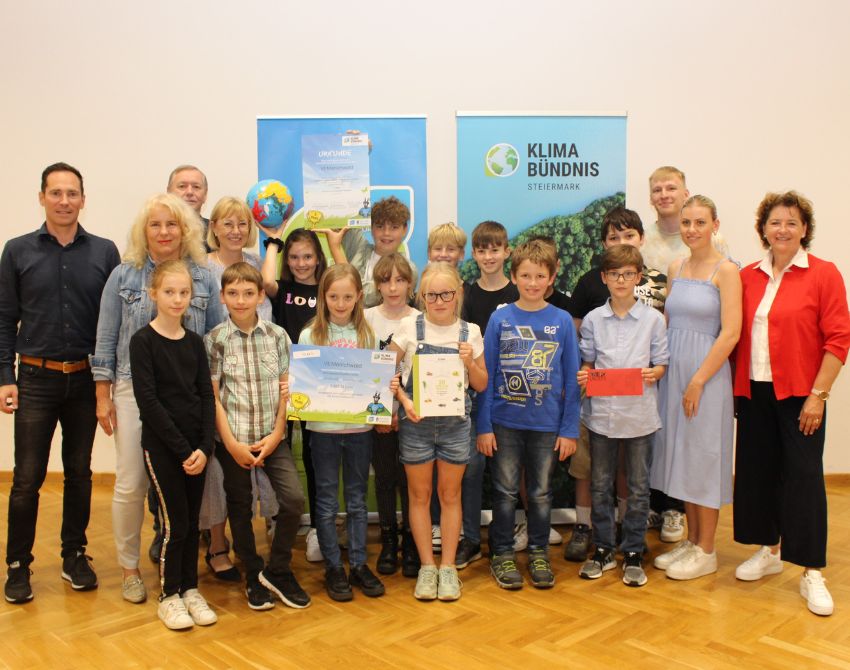 Gruppenbild von Kindern mit Urkunden, einem großen Scheck und Gutscheinen in der Hand, und einem Fußball, mit Erwachsenen am Bildrand, dahinter zwei Roll-Ups