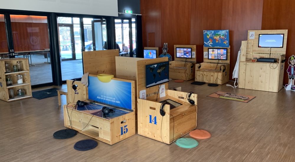 Ausstellungsboxen in einem großen Raum mit Bildschirmen und Kopfhörern