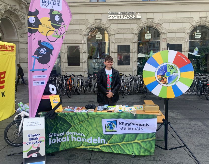 Infostand mit Quizrad und jungem Mann hinter Infotisch